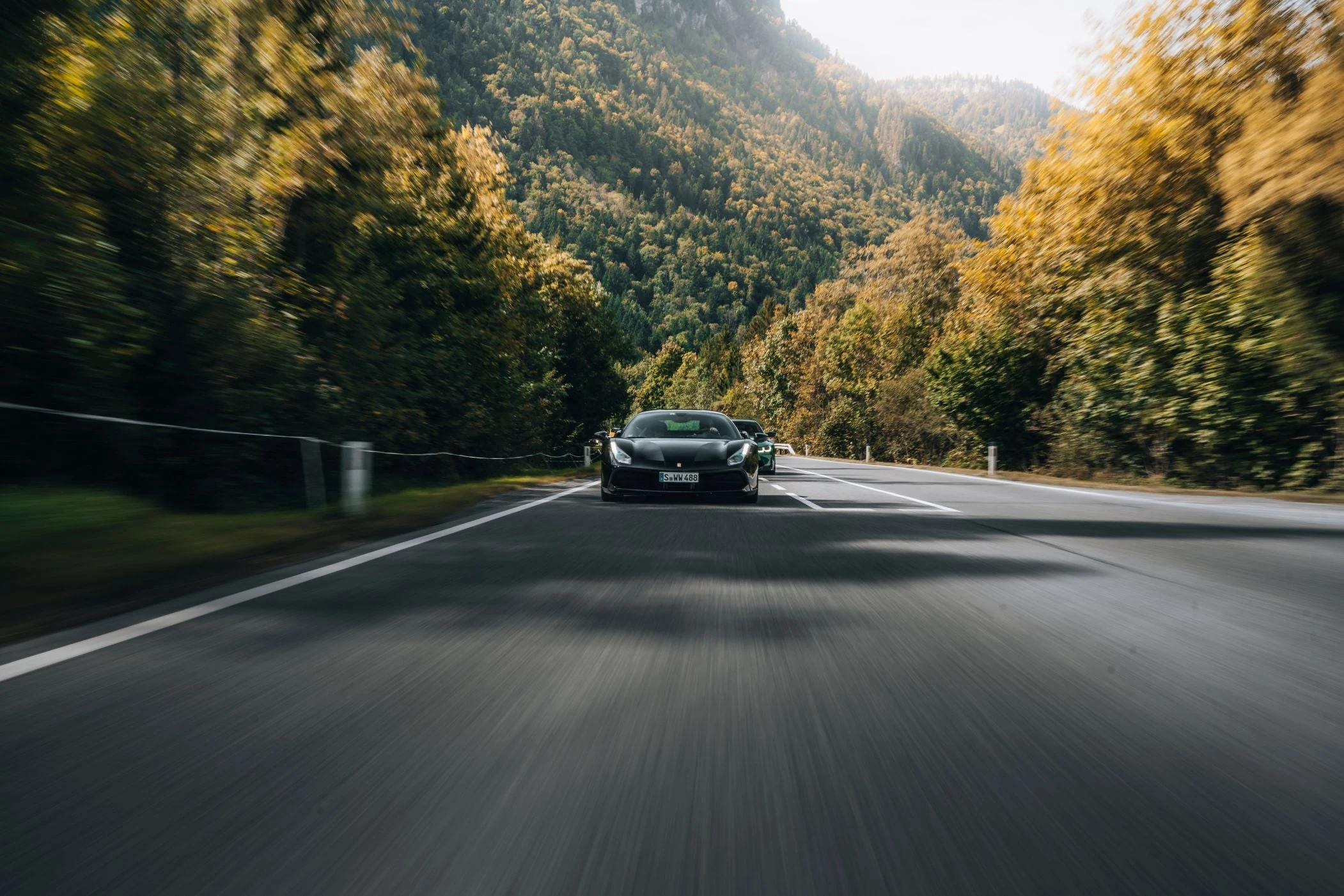 Ferrari in Fahrt vor herbstlicher Alpenlandschaft